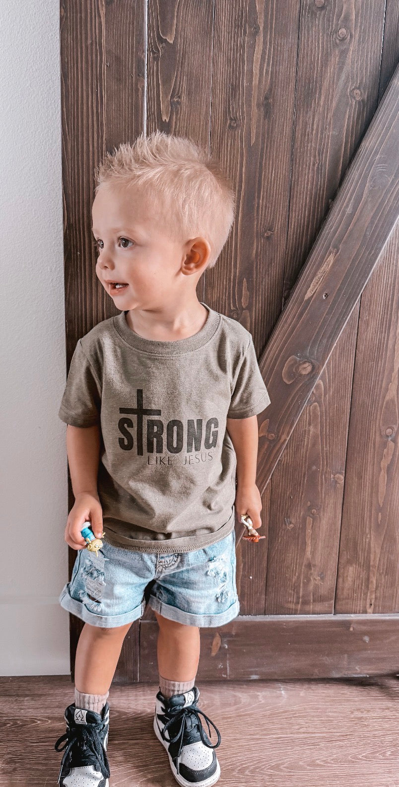 Young boy wearing Strong Like Jesus olive green toddler t-shirt